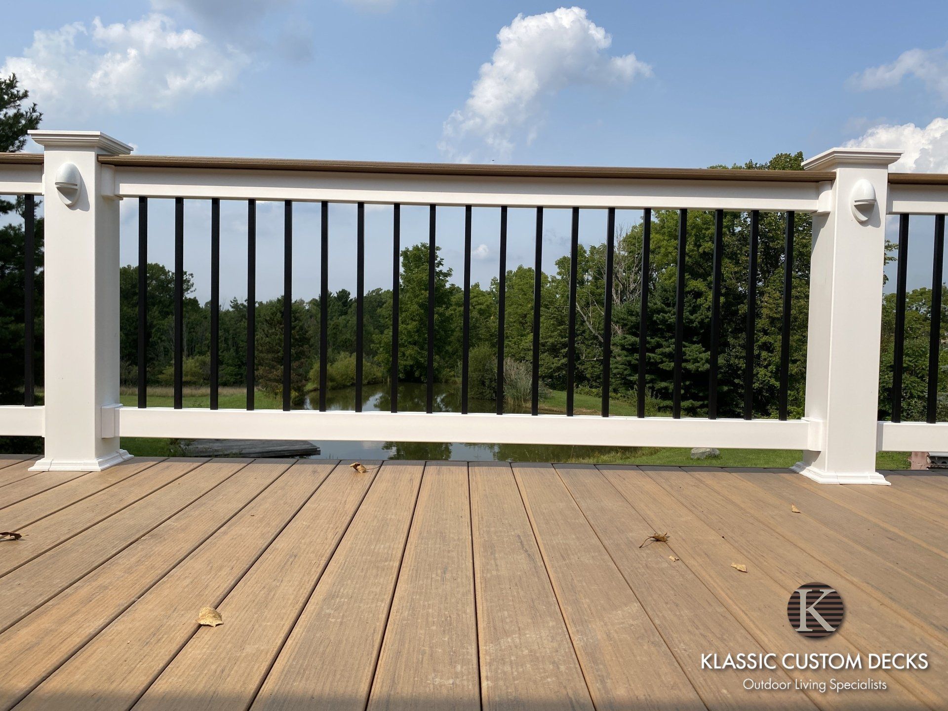 White railing with black balusters on a wood deck, overlooking green trees and a blue sky