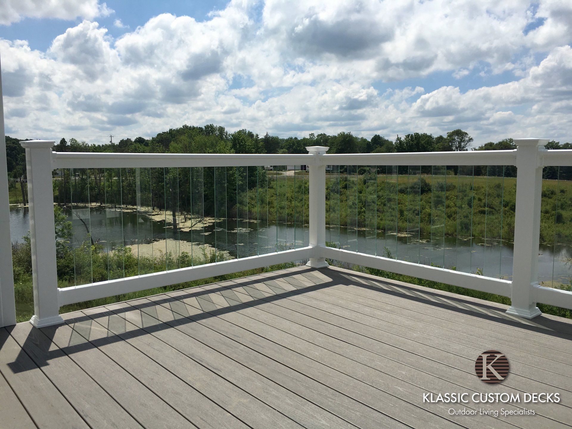 White deck railing overlooking a green lake under a cloudy sky