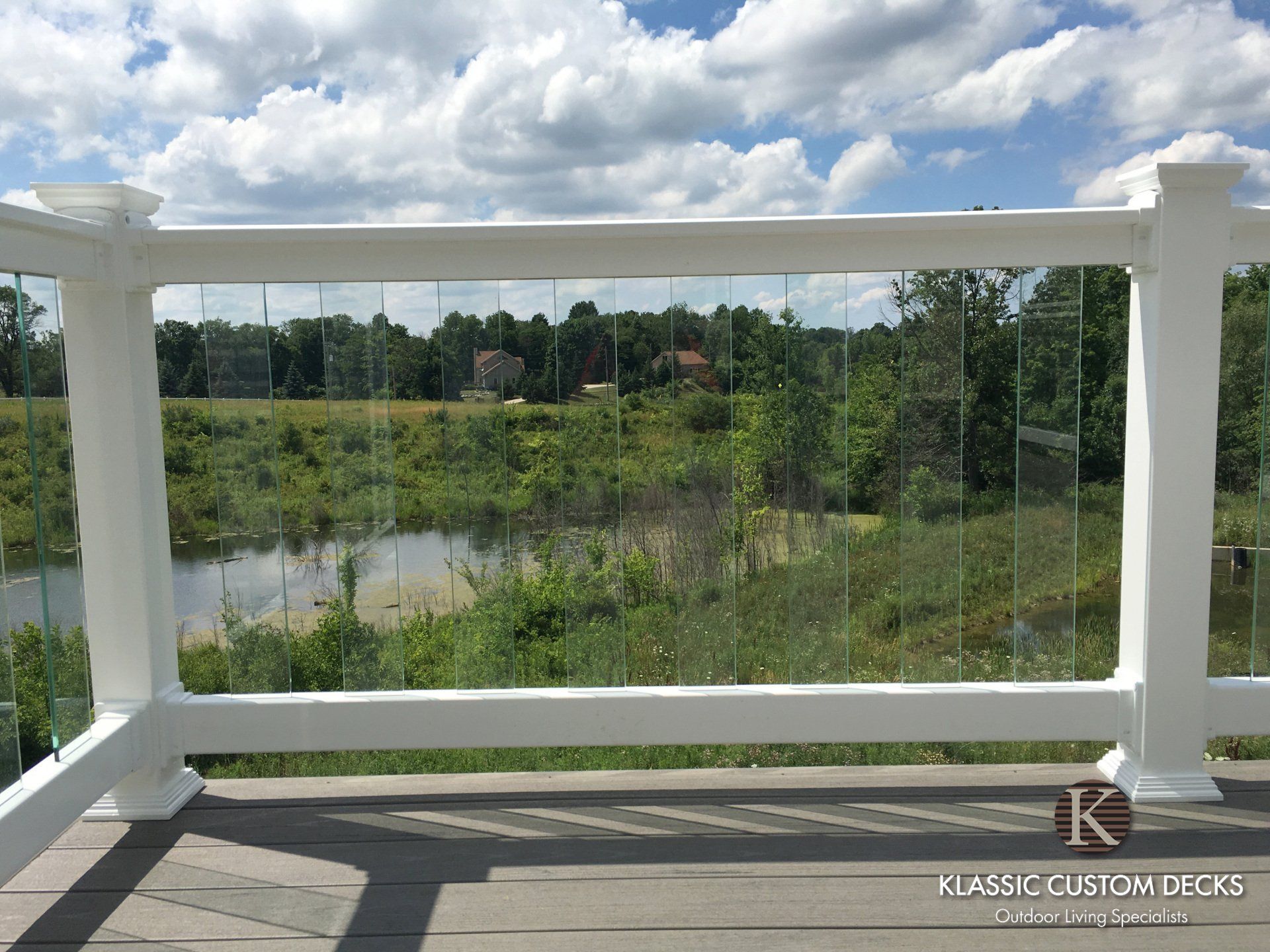 White balcony railing overlooking a pond, green field, and cloudy sky.