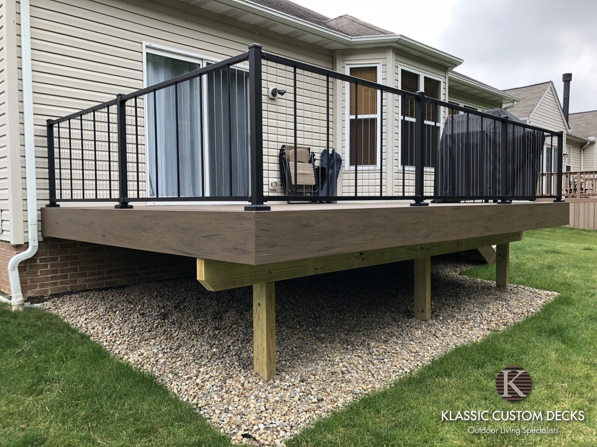 Back deck with black railing, gray privacy curtains, and a gravel foundation in a suburban yard