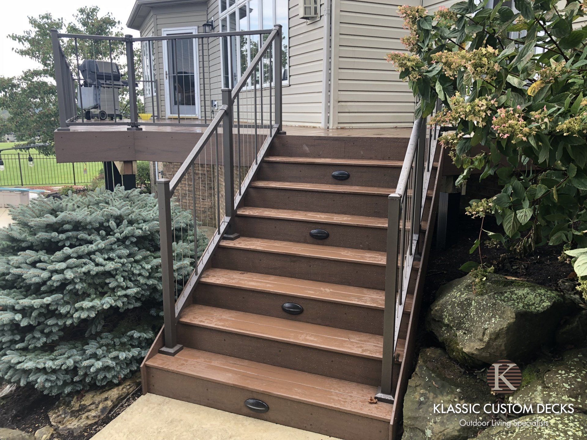 Front porch stairs with brown steps, metal railings, and landscape shrubs beside a house