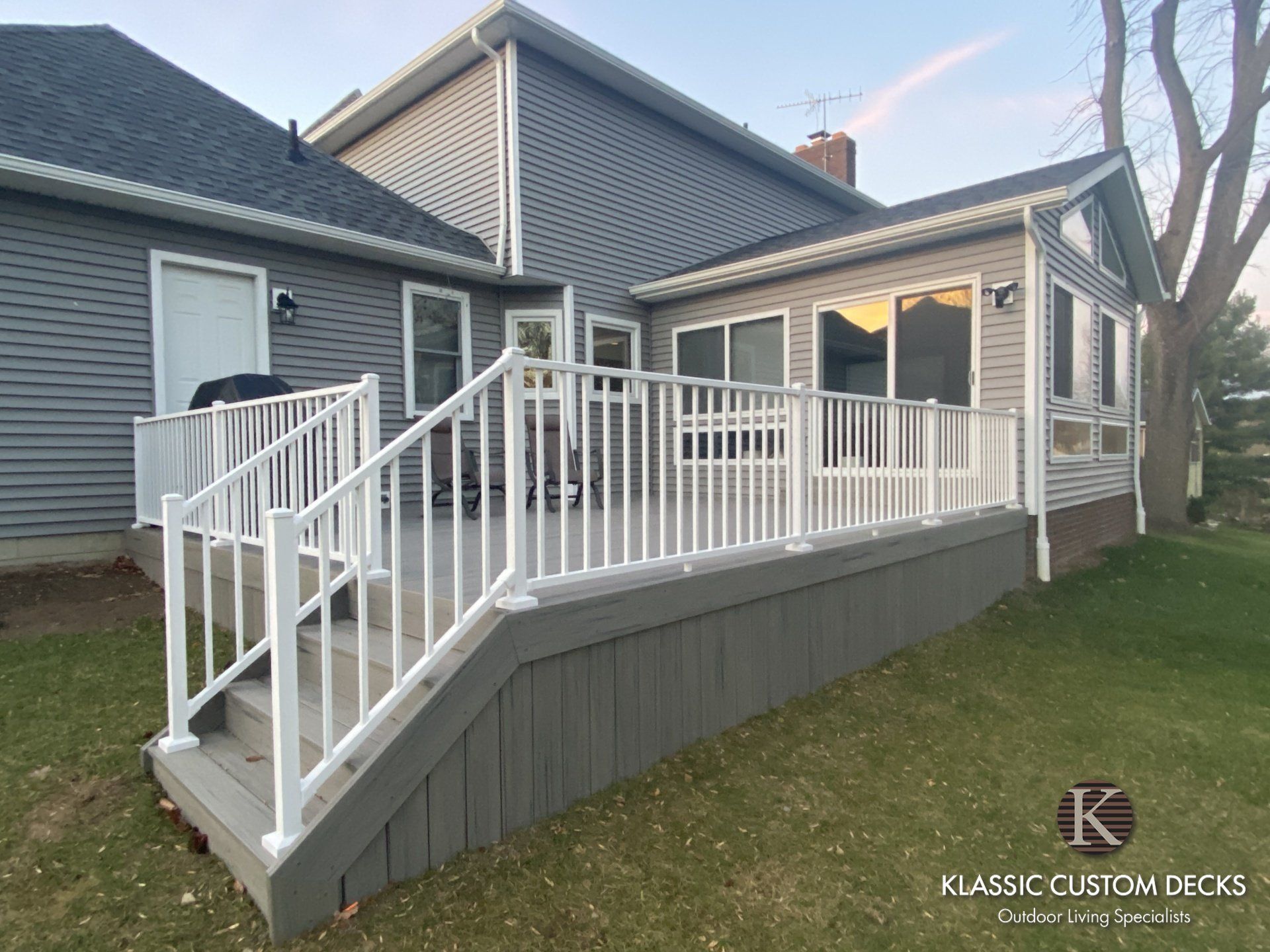 White wheelchair ramp with railings attached to gray house and deck in a yard