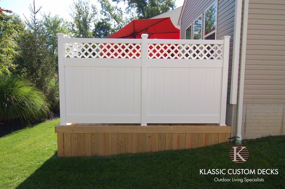 White privacy deck with lattice top beside a house, featuring wood steps and red patio umbrellas