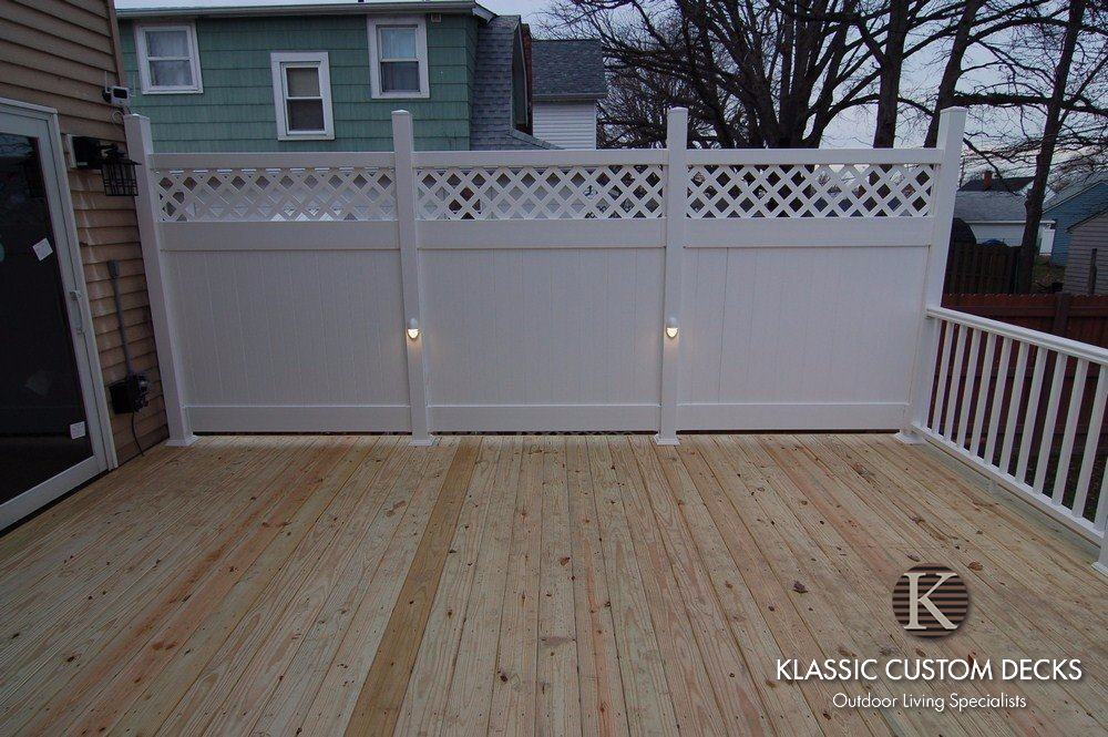 Wooden deck with cream privacy fence and white railings beside a house