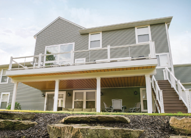 Two-story gray house with white trim, front deck, and exterior staircase on a rocky hillside.