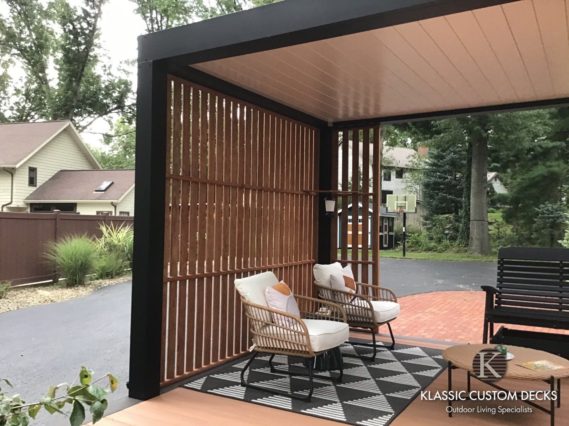 Modern outdoor patio with lounge chairs, a black-framed pergola, wood slat walls, and a patterned rug