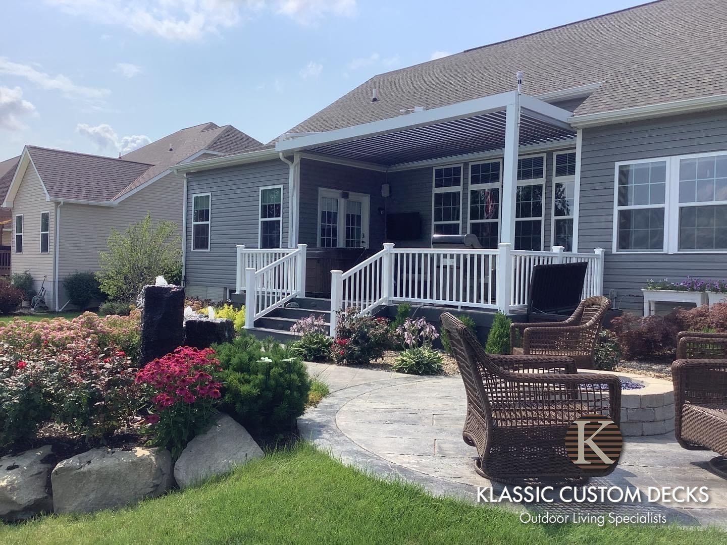 Front porch of a gray house with white railings, stone walkway, and landscaped flower beds