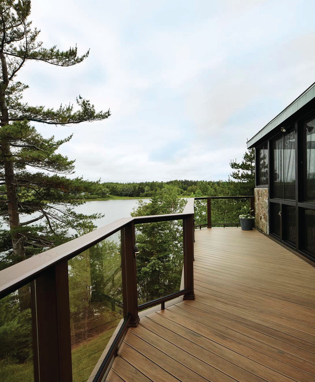 Wooden deck overlooking a lake and pine trees beside a cabin under a cloudy sky