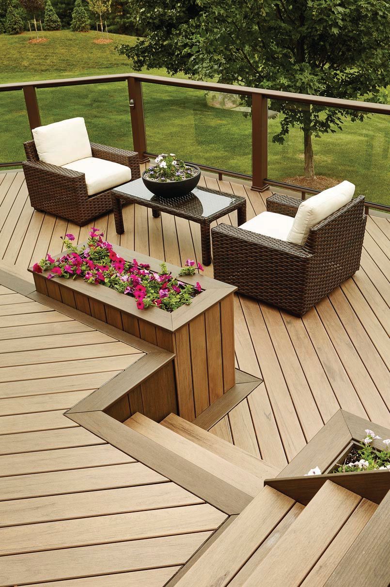 Wooden deck with wicker patio chairs, small table, and flower planter overlooking a green yard