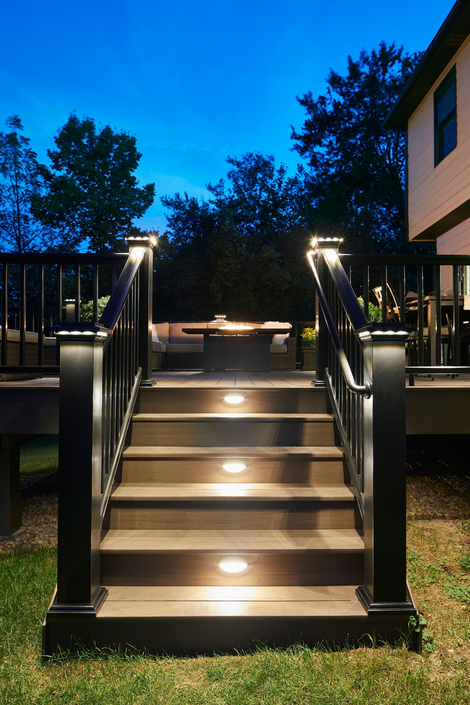 Lit outdoor staircase with black railings leading to a raised walkway at dusk