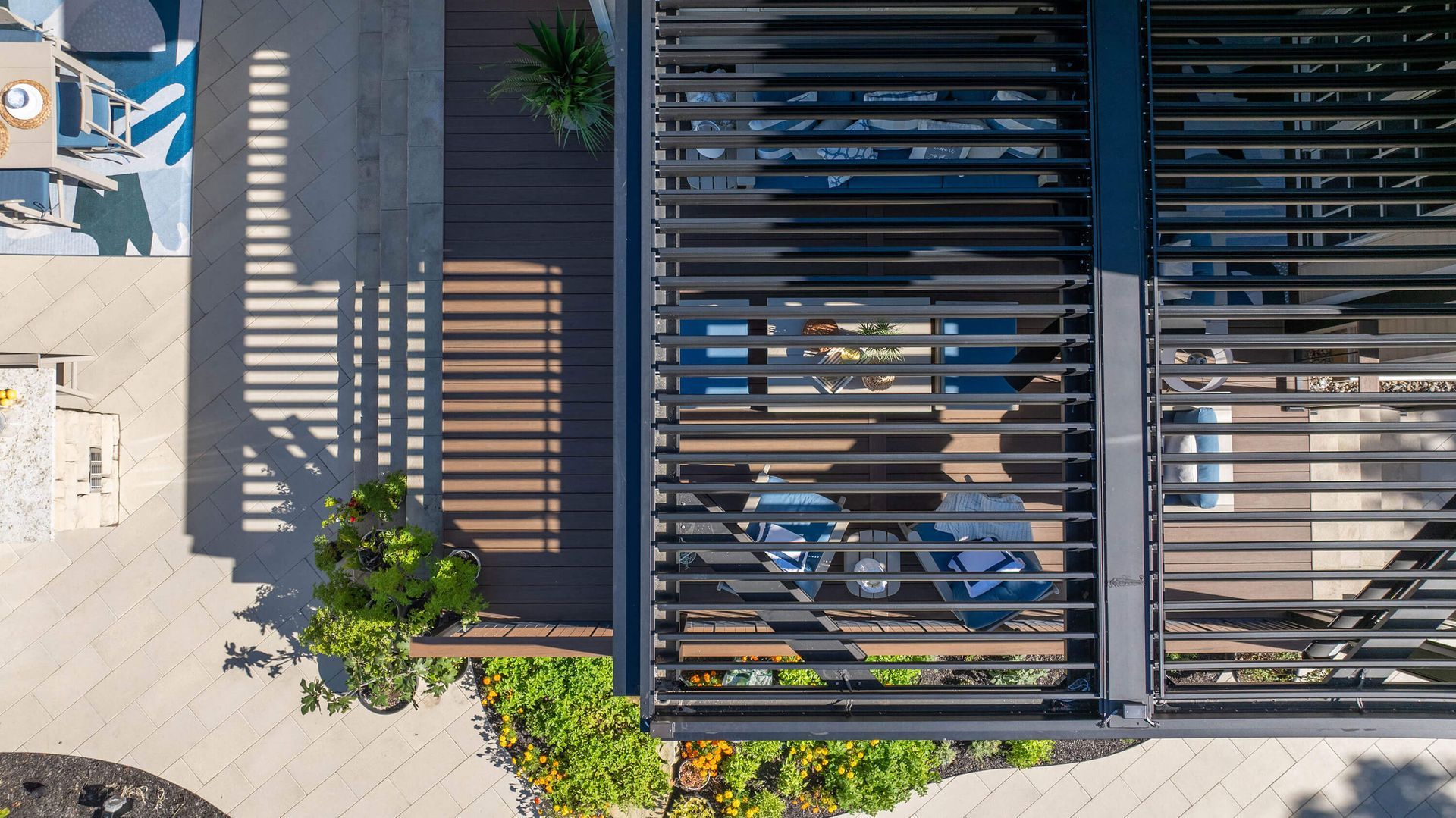 Aerial view of a modern building with dark slatted roof, patio seating, and surrounding greenery