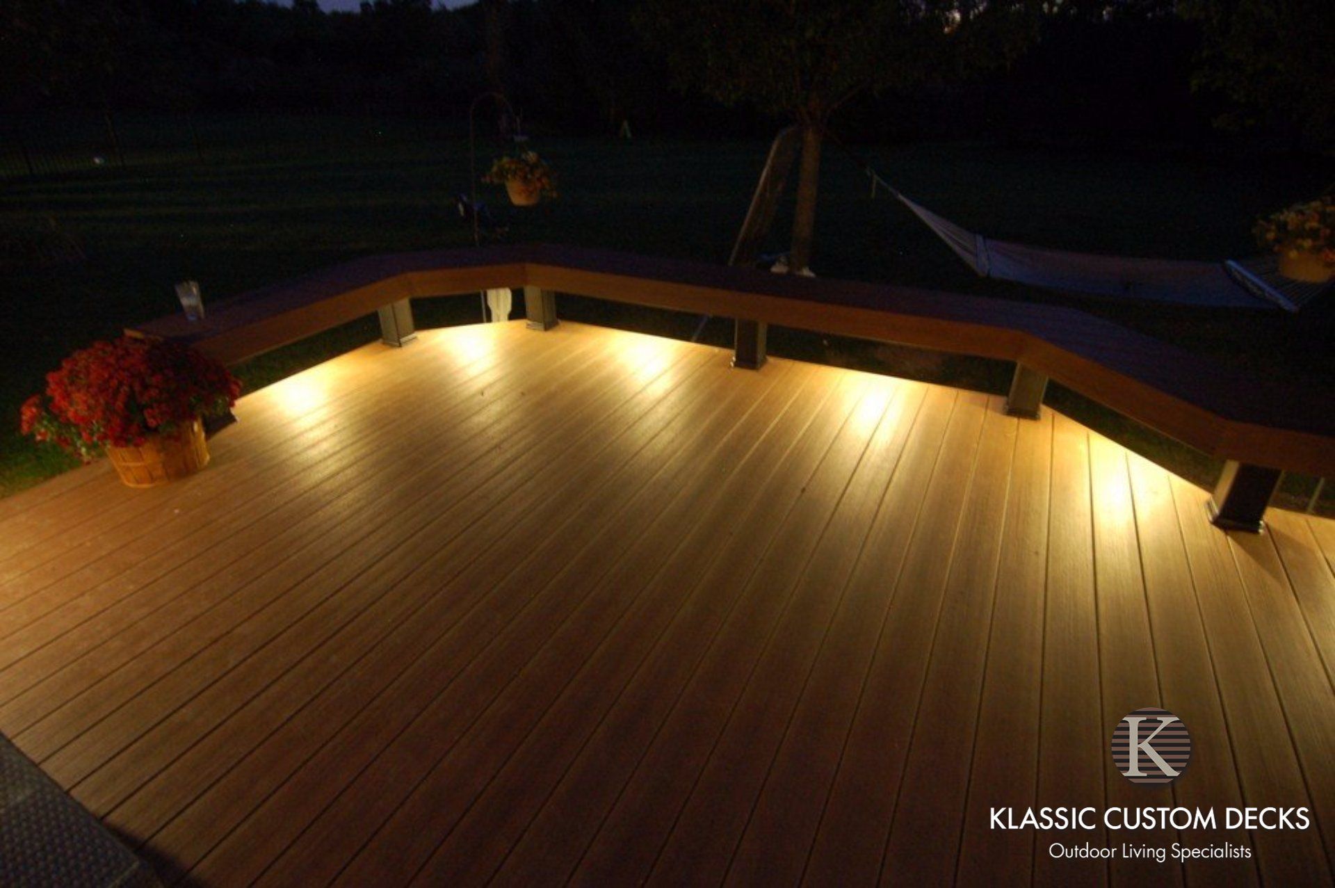 Warmly lit wooden deck at night with curved railing and surrounding darkness