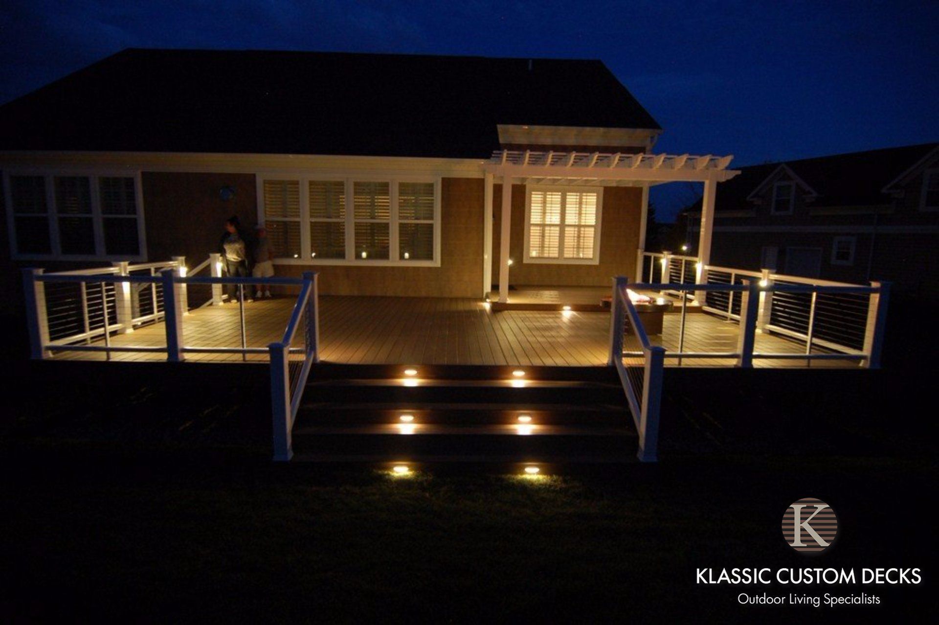 Deck with lit steps and railings at night, in front of a house.