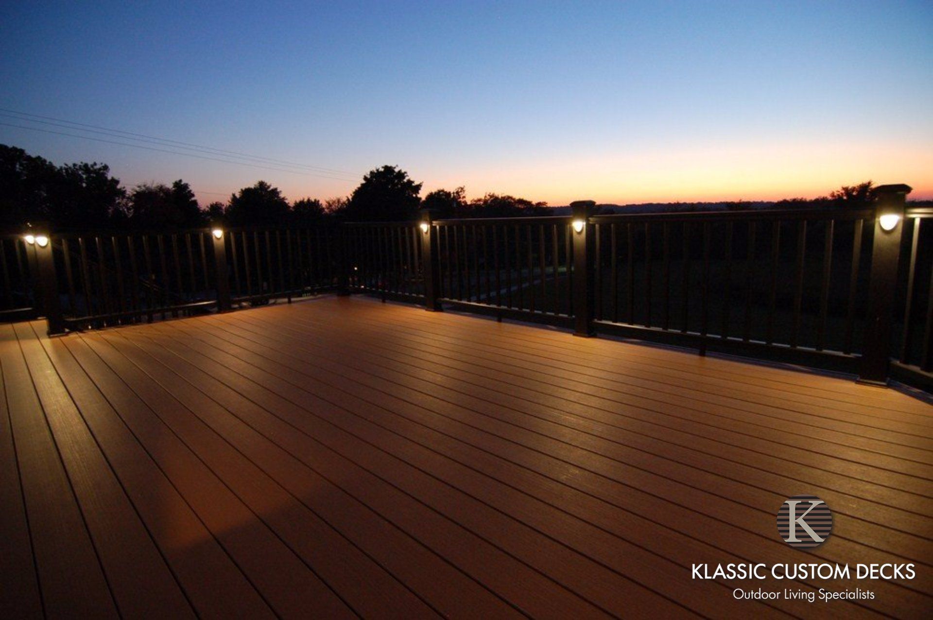 Wooden deck with black railings at sunset, overlooking a dark landscape and glowing horizon