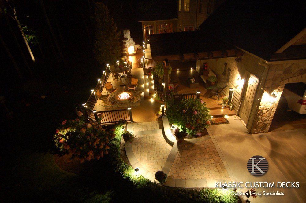 Nighttime backyard patio with warm landscape lighting, stone paths, and outdoor seating areas.