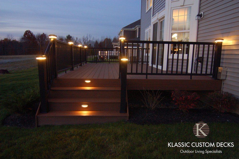 Lit backyard deck with steps, railing lights, and a lit house at dusk.