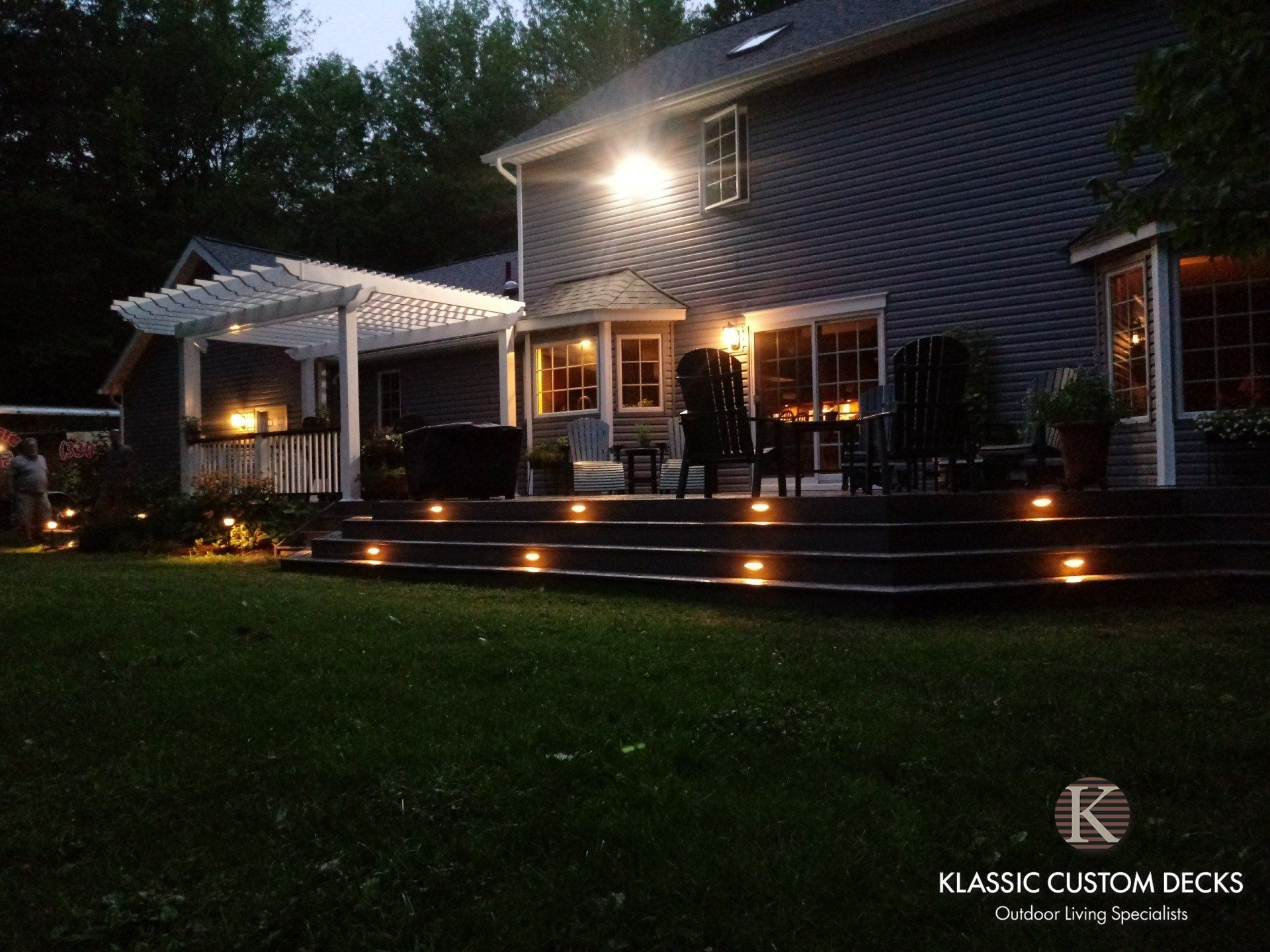 Nighttime backyard patio with lit steps, covered seating area, and house exterior lights on.