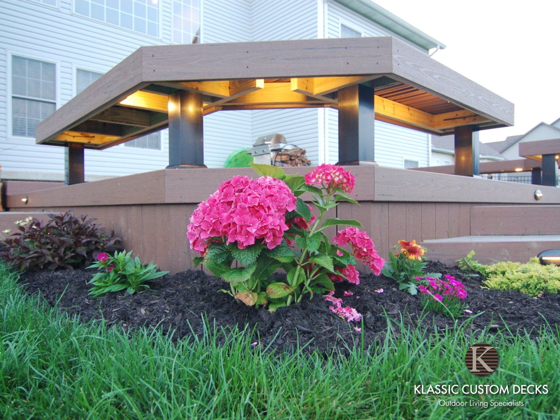Modern pavilion with warm lights and pink flowers in a landscaped garden at dusk