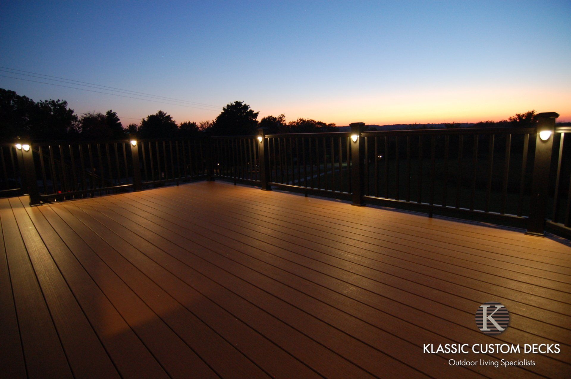 Wooden deck at dusk with black railing and warm path lights under a fading sunset sky