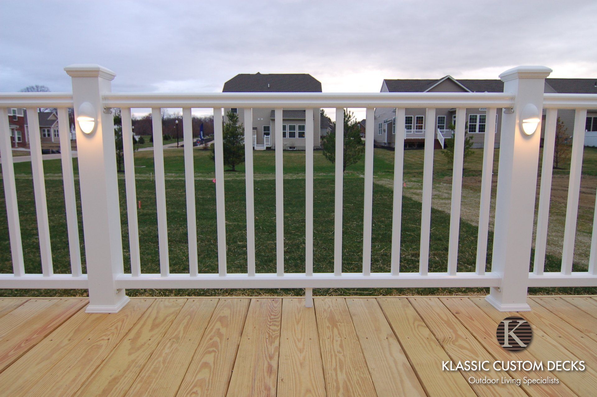 White railing on a wooden deck overlooking a green lawn and house at dusk