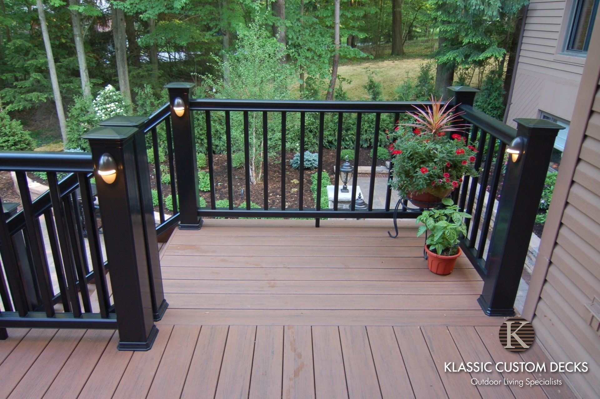 Wooden deck with black railing and potted flowers overlooking a wooded yard