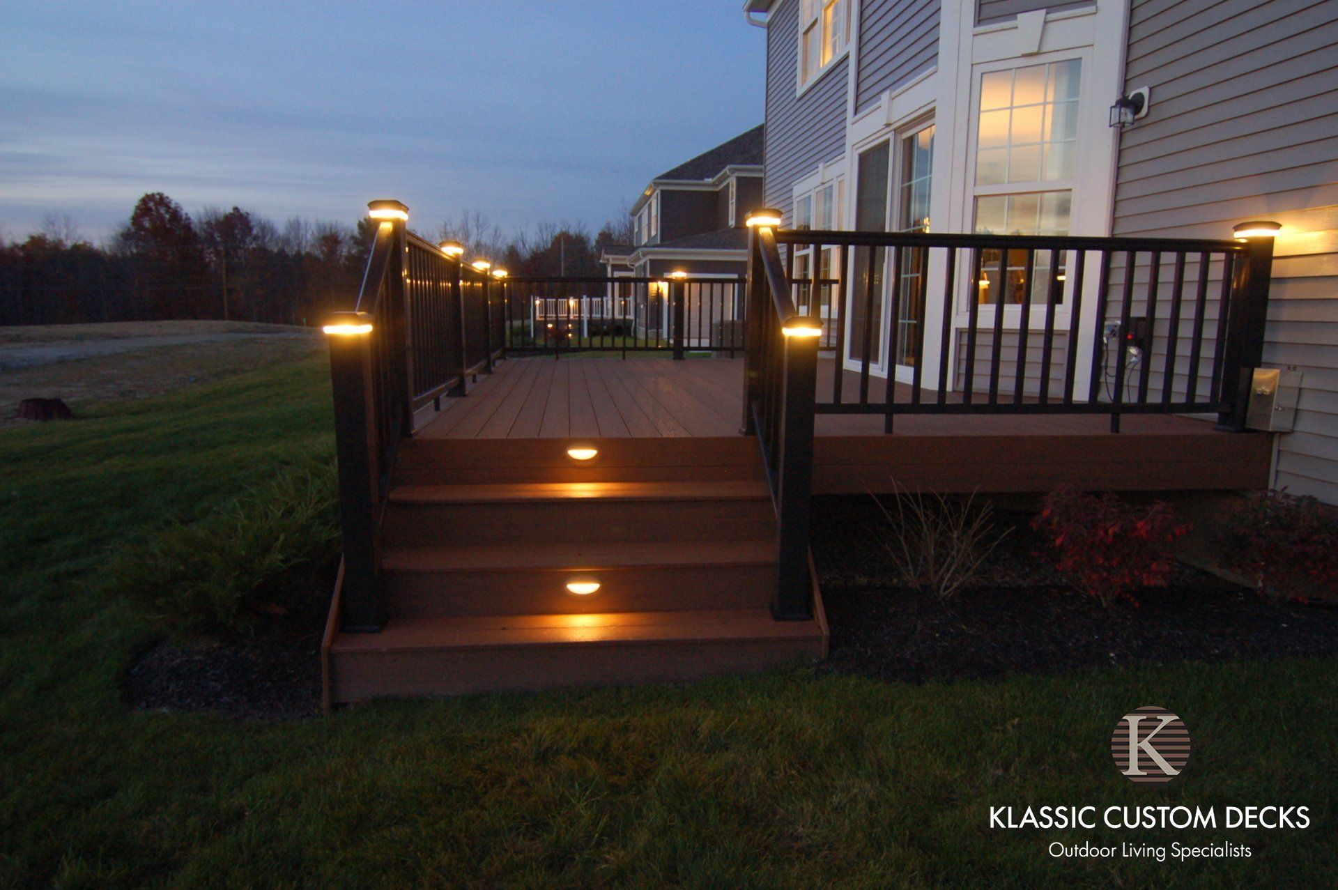 Back deck stairs with lit step lights leading to a house at dusk