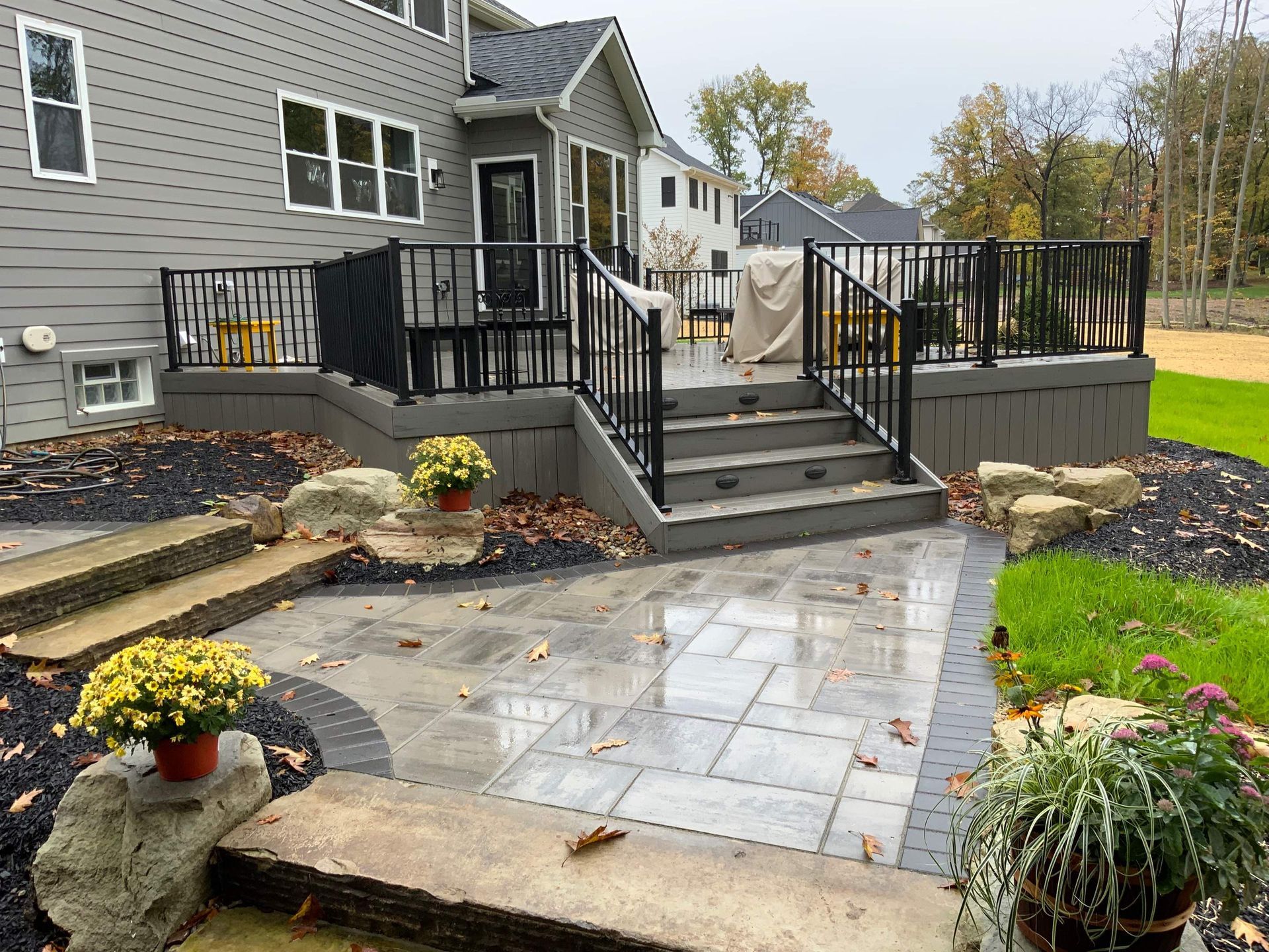 Back patio with black railings, stone steps, paver walkway, and landscaped garden beds