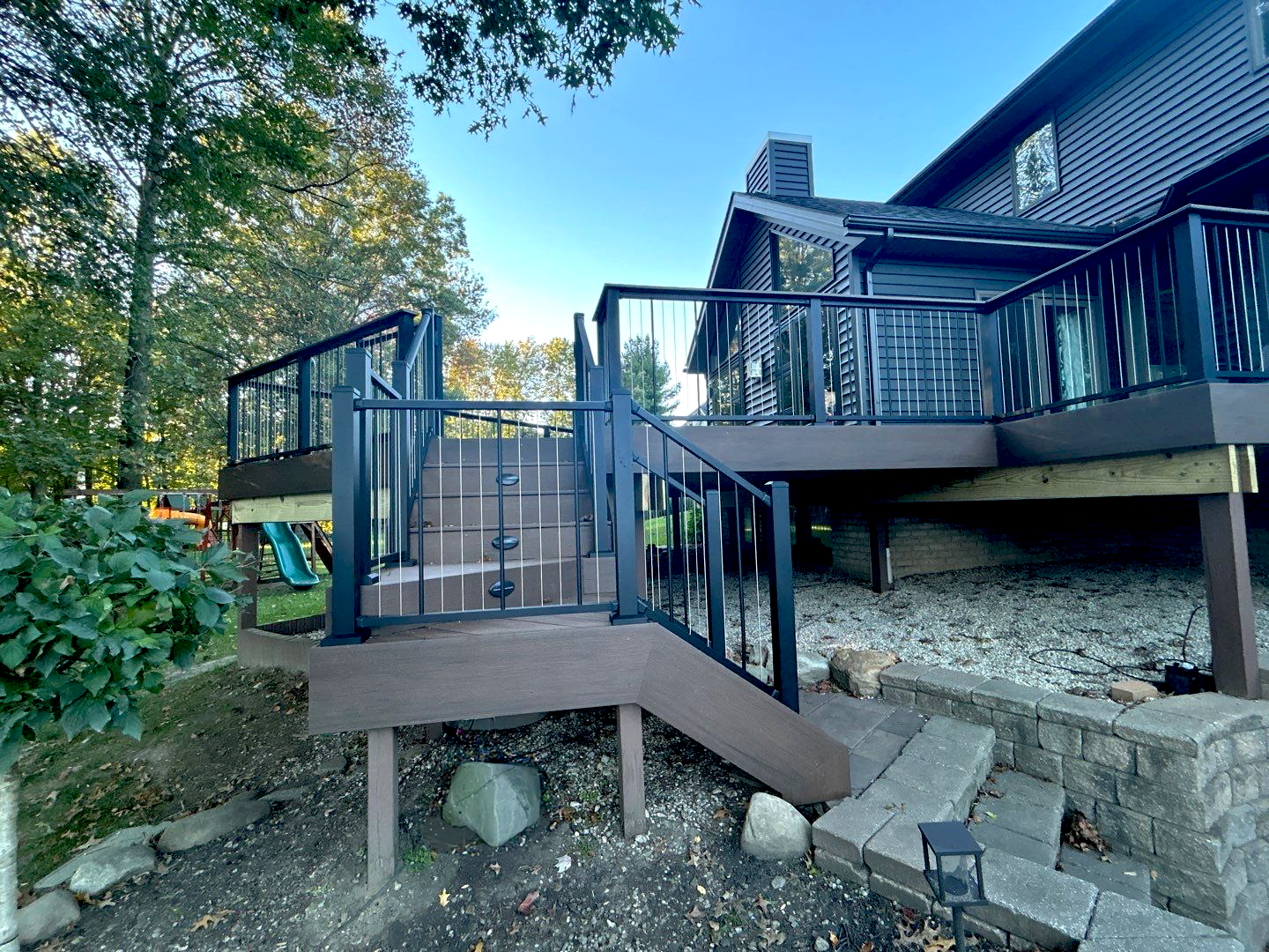 Wooden deck stairs and railings leading to a raised porch beside a house in a leafy yard