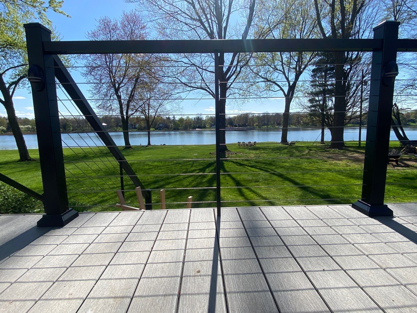 Black metal frame on a tiled patio overlooking a grassy riverside park and water under a clear blue sky
