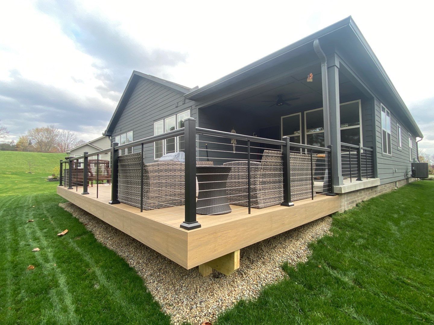 Modern gray house with a covered deck and black railing beside a green lawn.