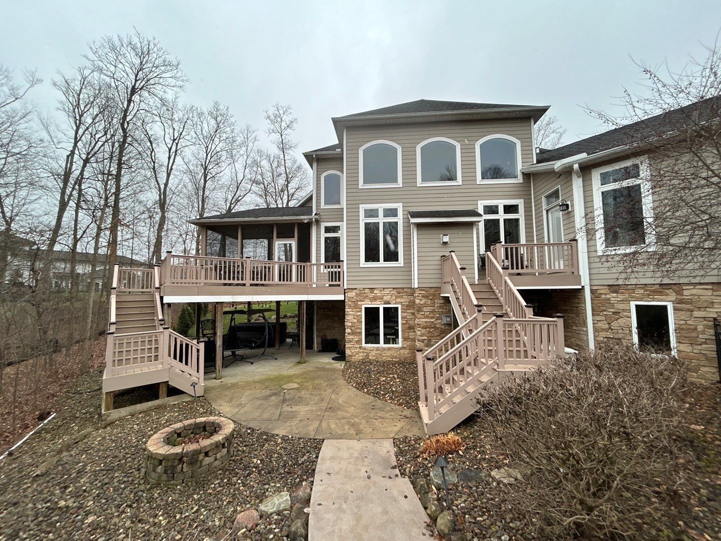 Backyard view of a raised deck with stairs attached to a gray two-story house