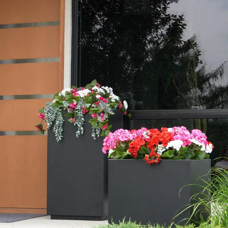 Two black planters with pink and white flowers beside a modern building entrance