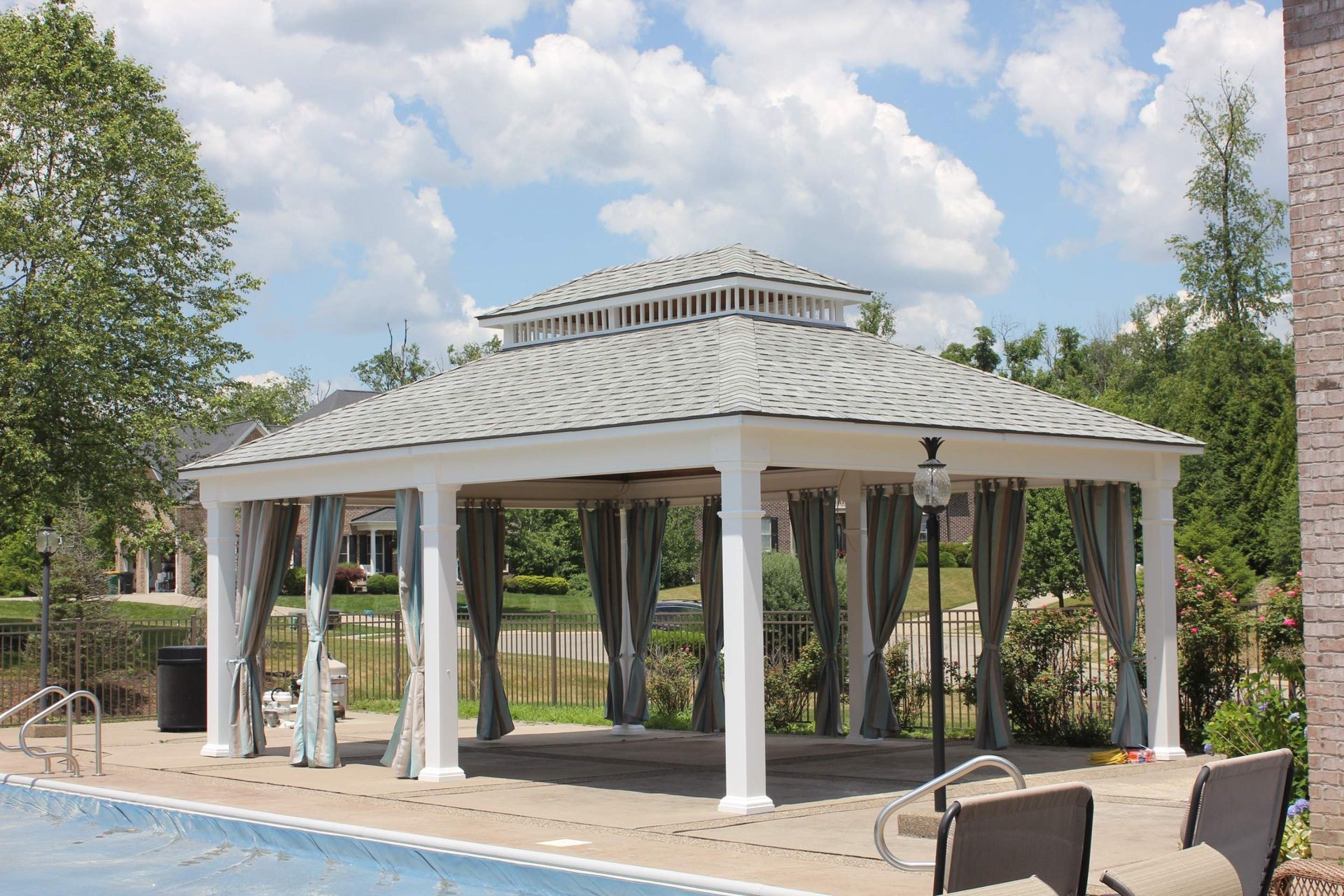 White pavilion by a pool with draped curtains, trees, and cloudy sky