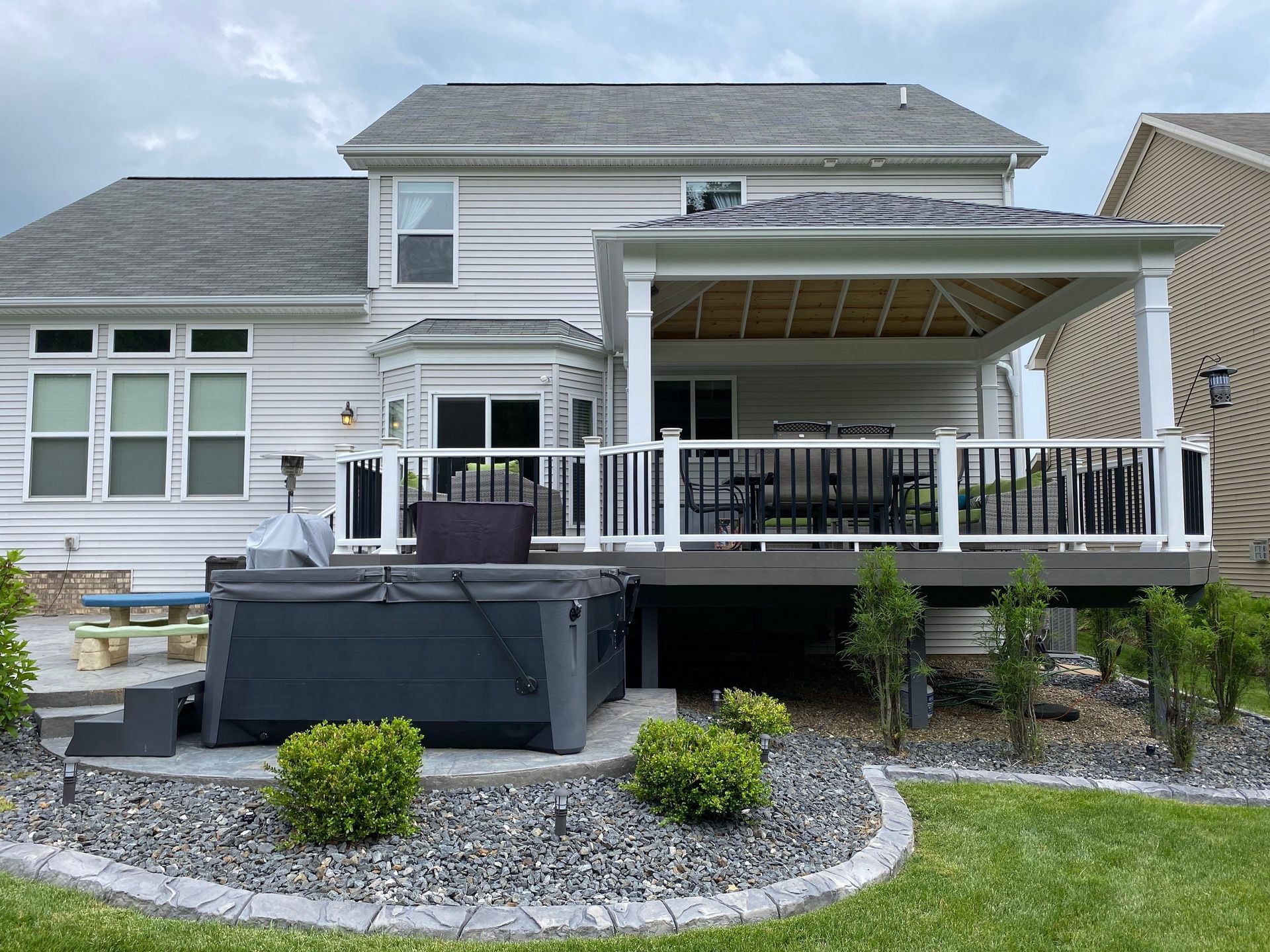 Backyard deck with pergola, hot tub, and patio seating beside a light gray house
