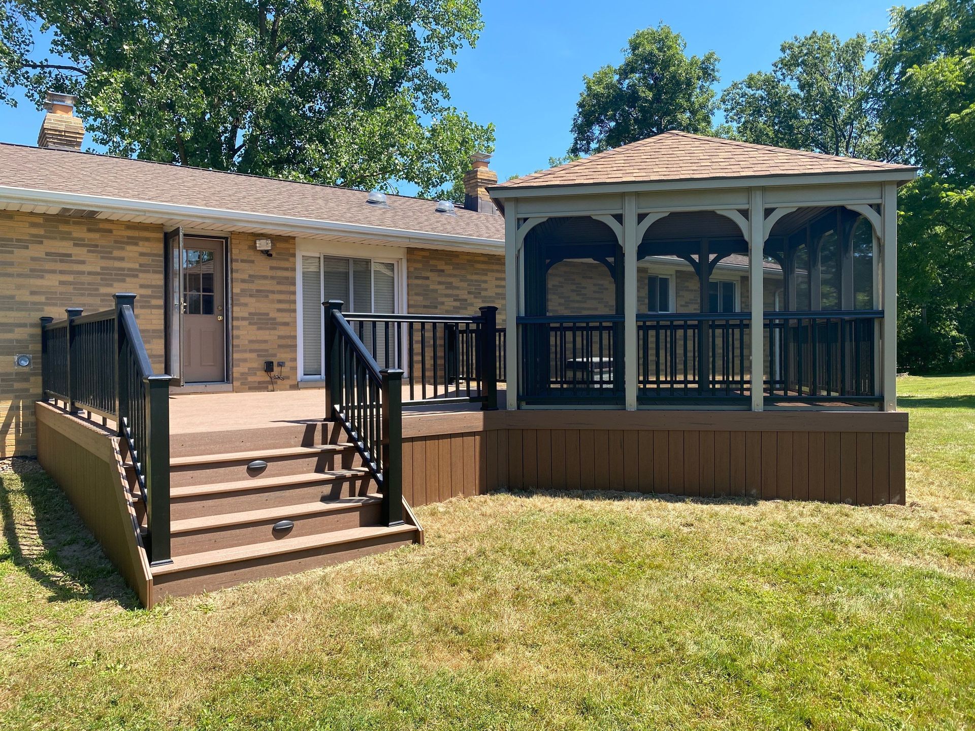 Backyard deck with steps, black railing, and a screened porch beside a house.