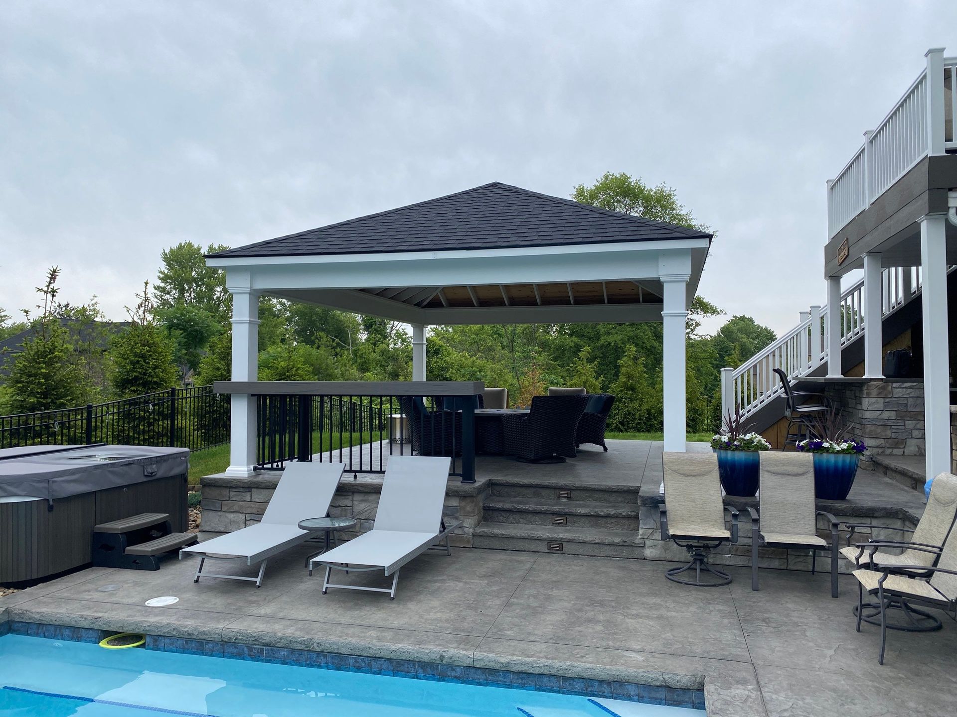 Backyard poolside gazebo with lounge chairs, hot tub, and stairs leading to an elevated deck
