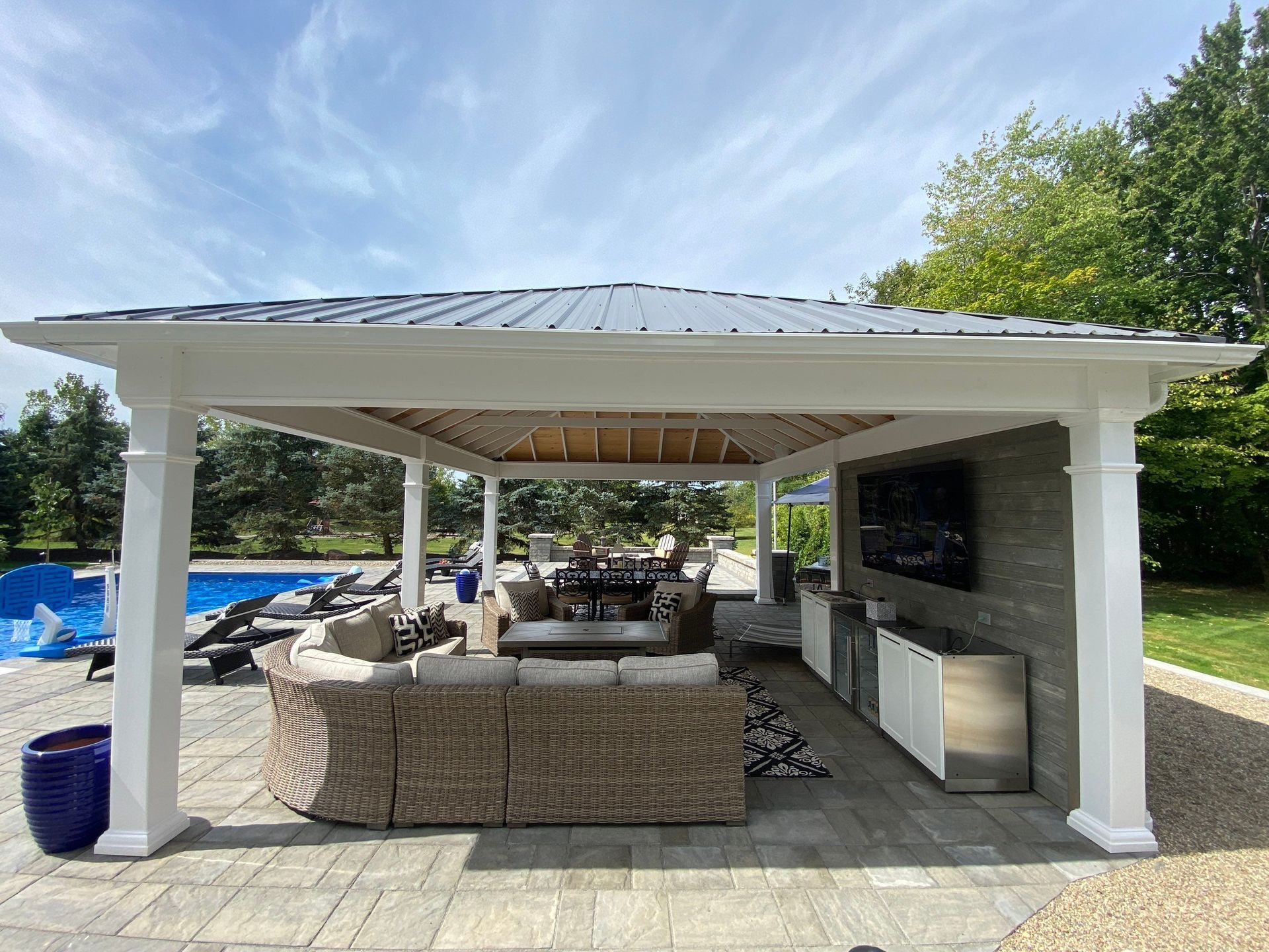 Outdoor patio seating under a white-roofed pavilion with wicker furniture and a wall-mounted TV
