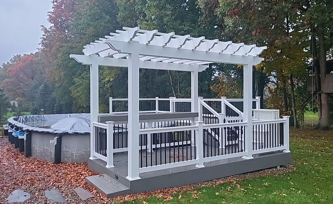 White pergola-covered pool deck with railings beside an above-ground pool in a leafy yard