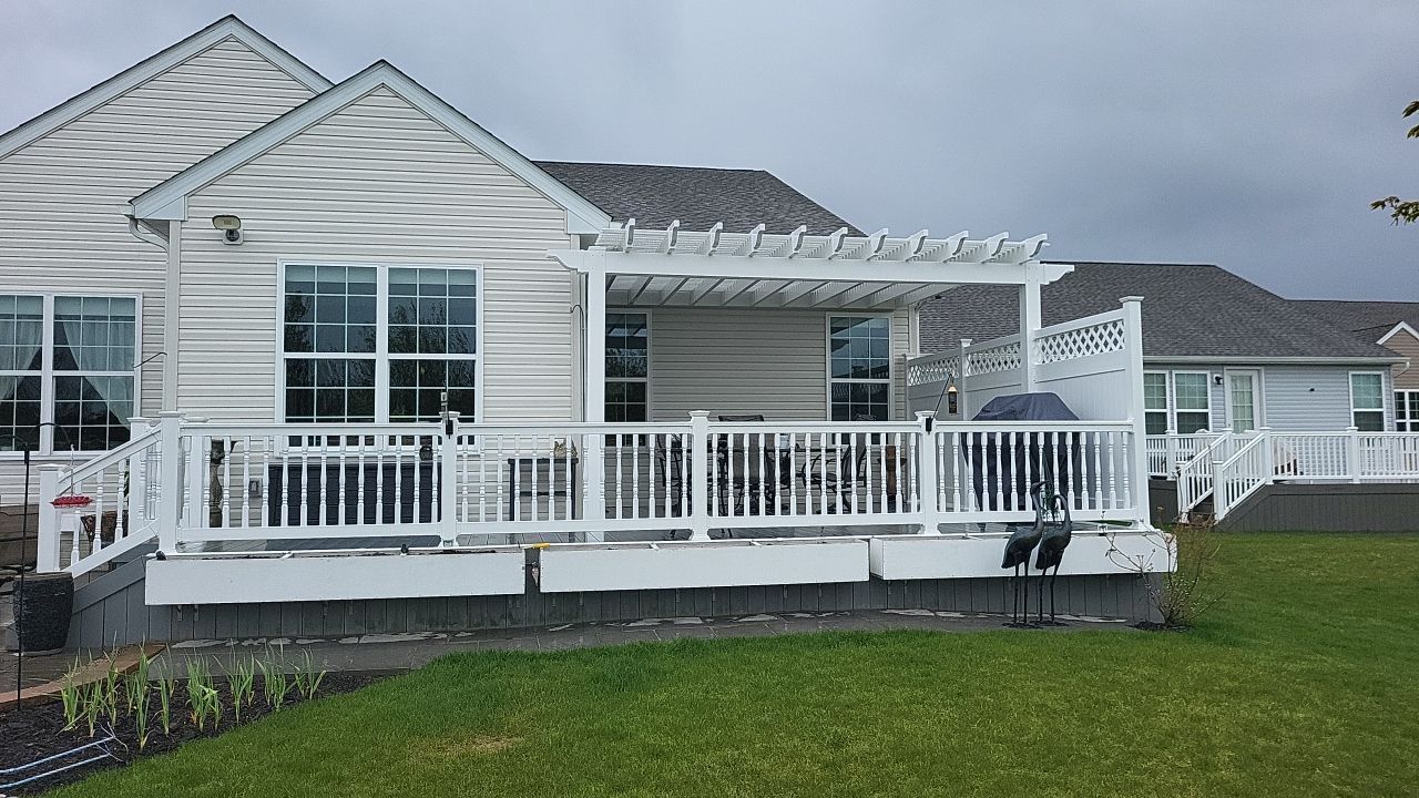 White house with a large front porch and railing on a grassy lot under a cloudy sky