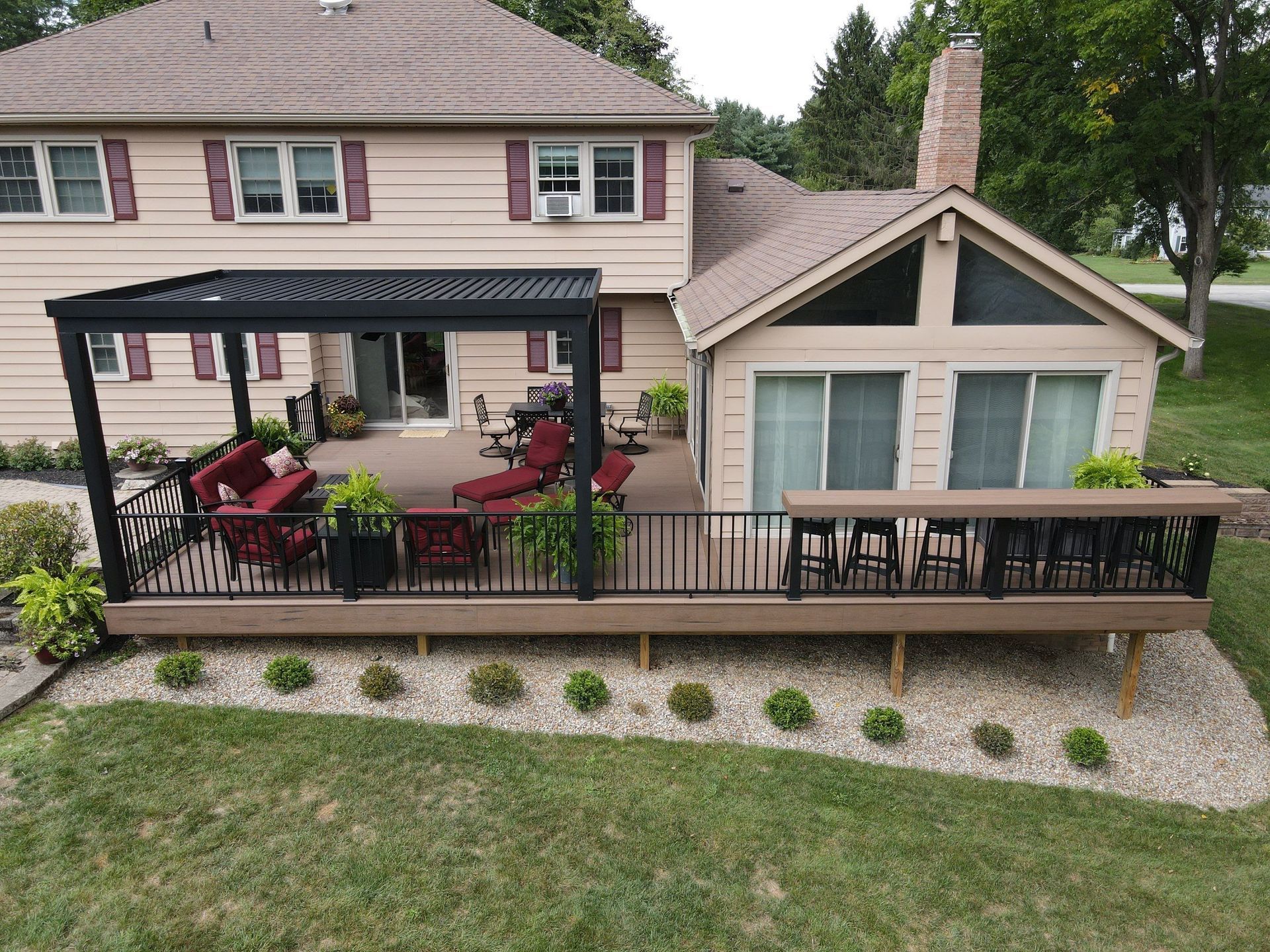 Backyard patio with pergola, red chairs, and a raised deck beside a beige house.