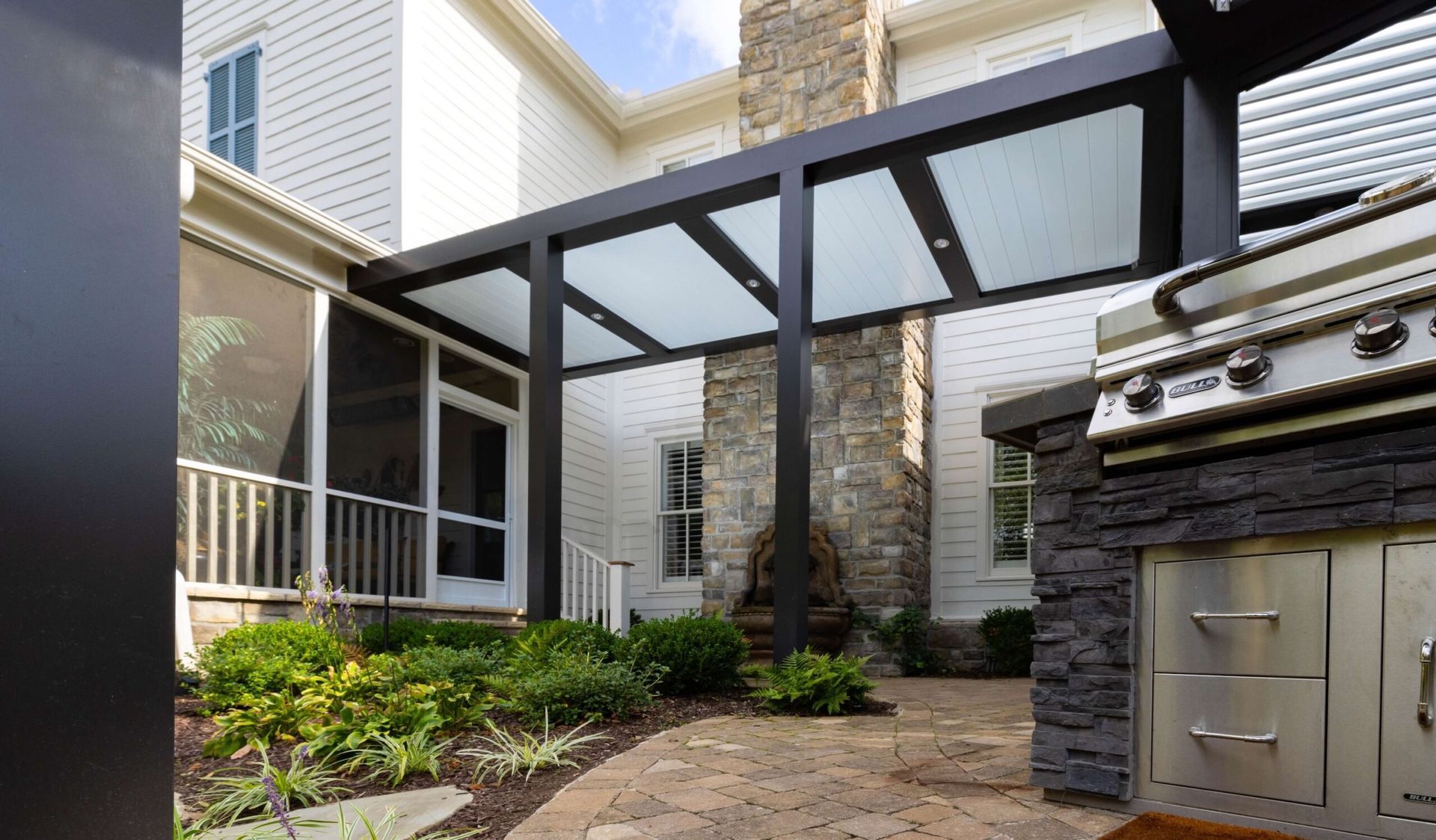 Modern apartment courtyard with patio paving, landscaping, and a black pergola over a walkway