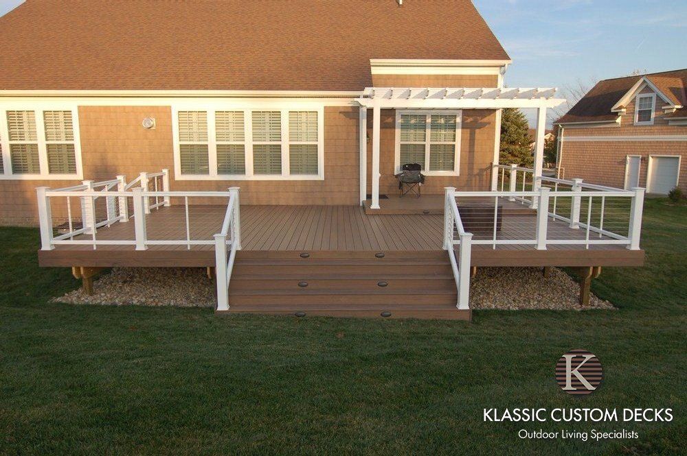 Custom wooden deck with white railings on a house exterior in a backyard setting