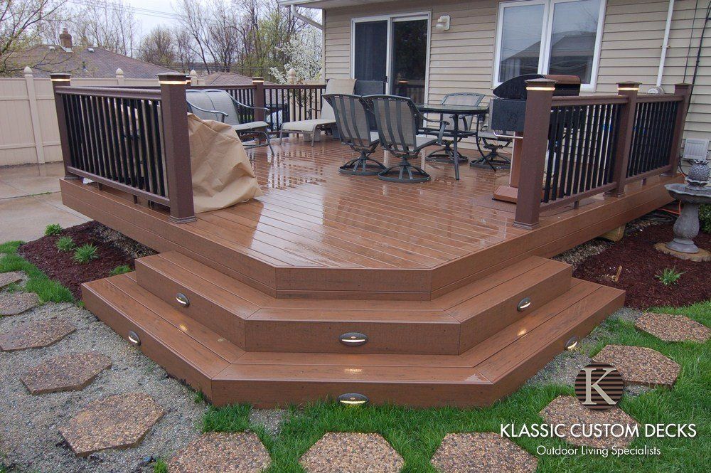 Brown multi-level deck with black railings and wet patio chairs outside a house