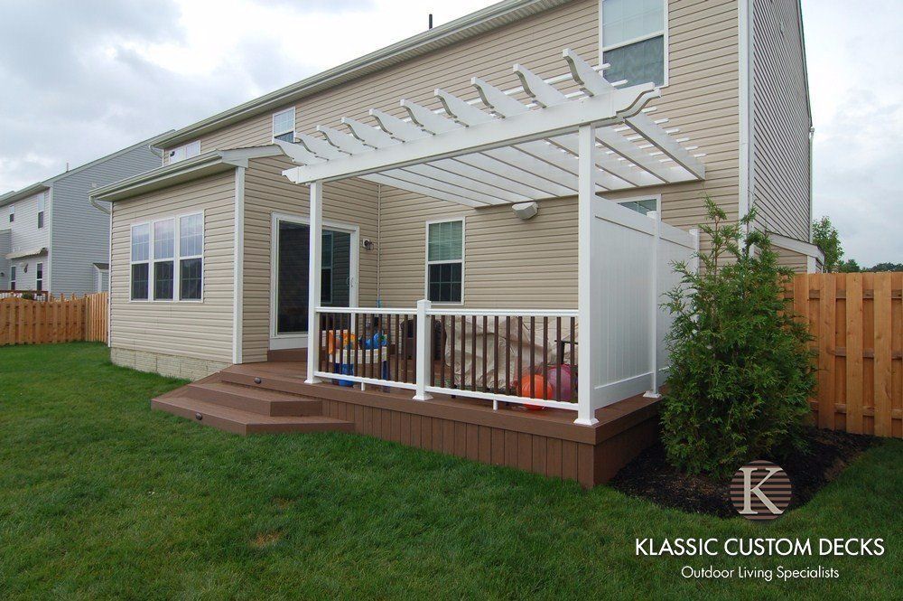 Backyard deck with white pergola, steps, railings, and wooden flooring beside a house
