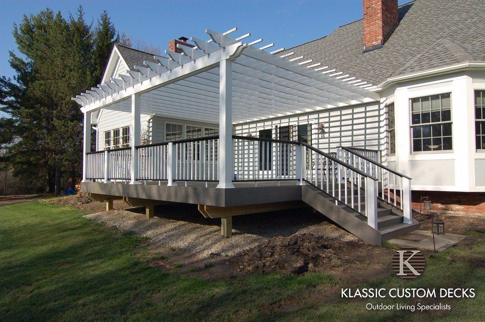 White porch deck with railings and steps attached to a house, beside a grassy yard.