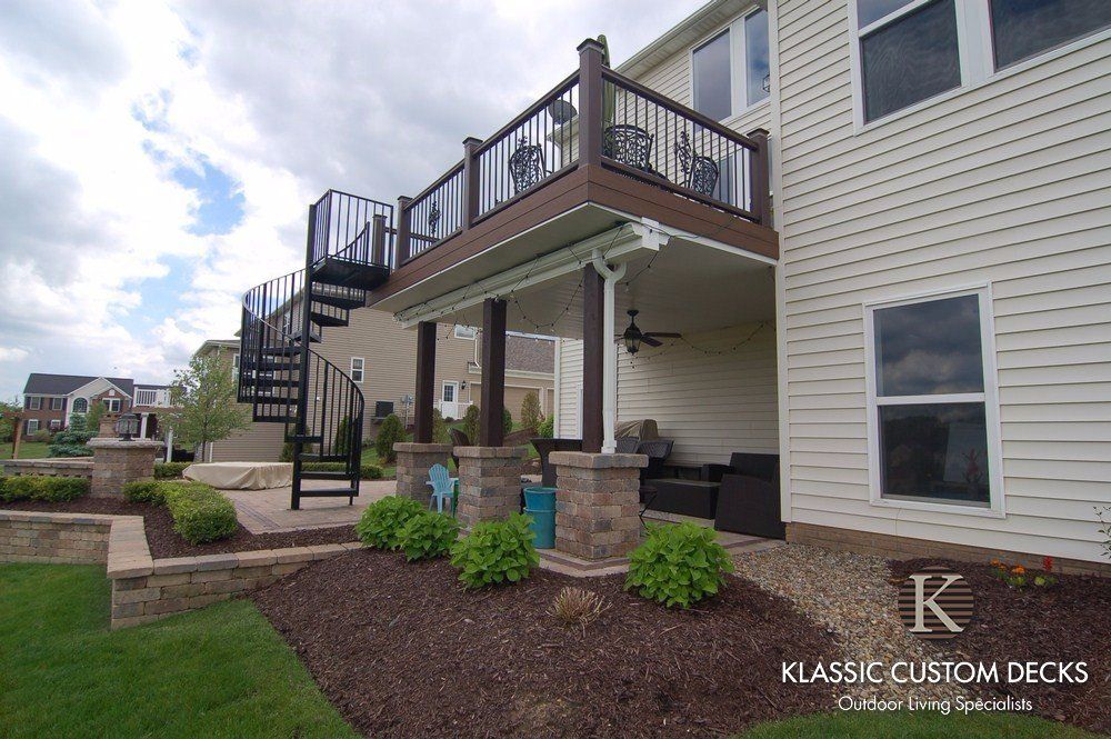 Two-story house with a raised wooden deck, staircase, and covered patio over a landscaped yard.