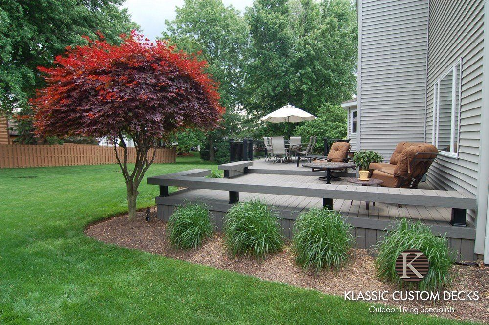 Backyard patio deck with outdoor seating, red Japanese maple, and landscaped shrubs beside a house