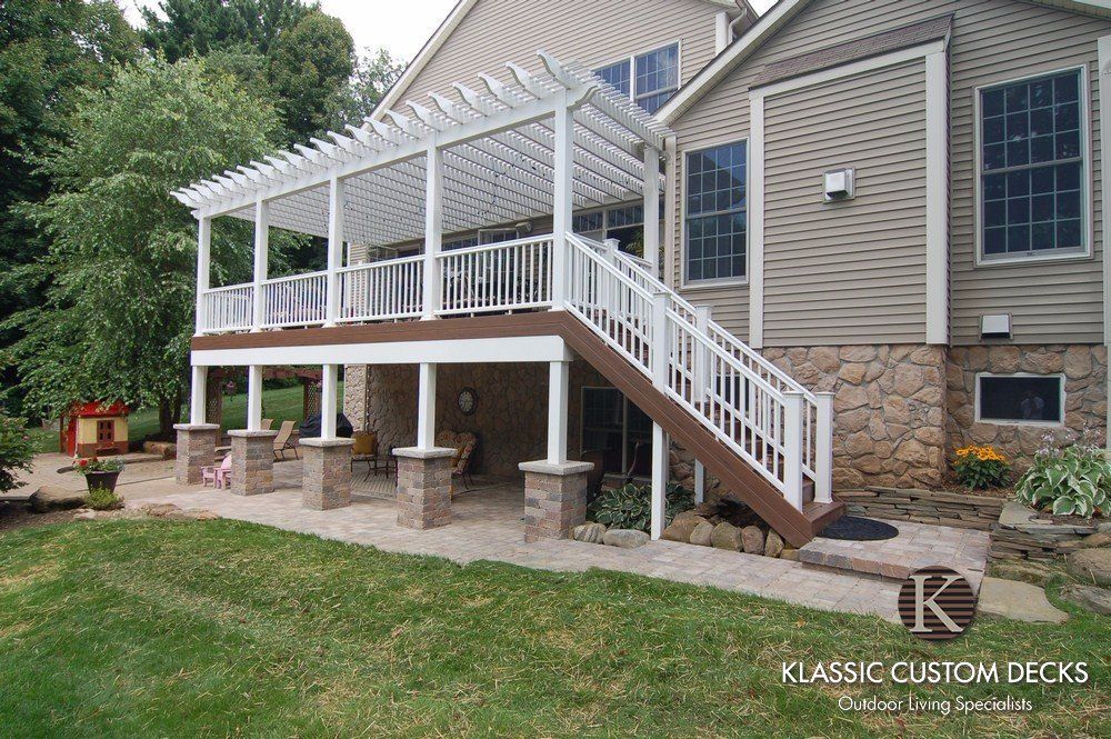 White pergola-covered deck with stairs attached to a beige house, overlooking a grassy yard