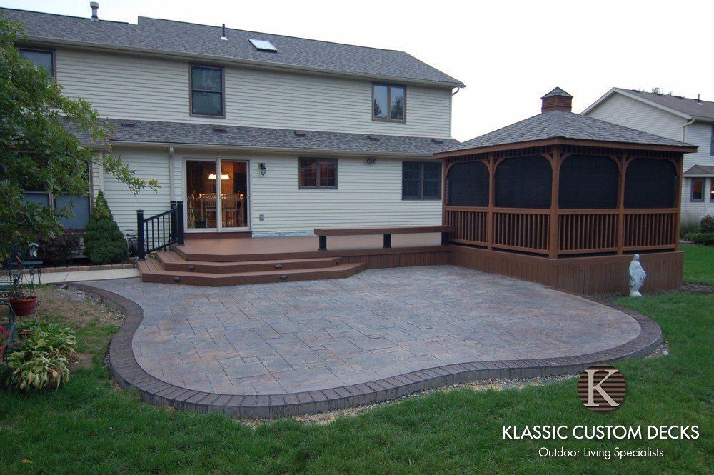 Backyard patio with large curved stone deck and wooden gazebo beside a two-story house