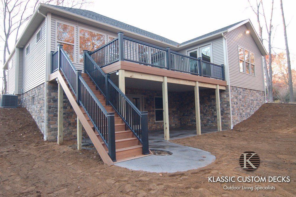 Raised wooden deck with stairs and black railings beside a house on a sloped yard